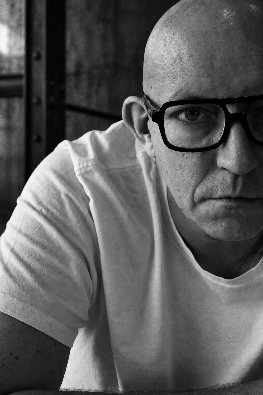 Portrait noir et blanc de Nick Dalk, lunettes sombres, devant un mur de béton.